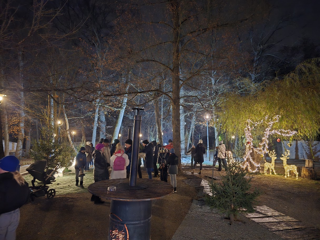 Leuchtende Rentiere unter einer mit Lichterkette geschmückten Baum, dahinter die Eisstockbahn